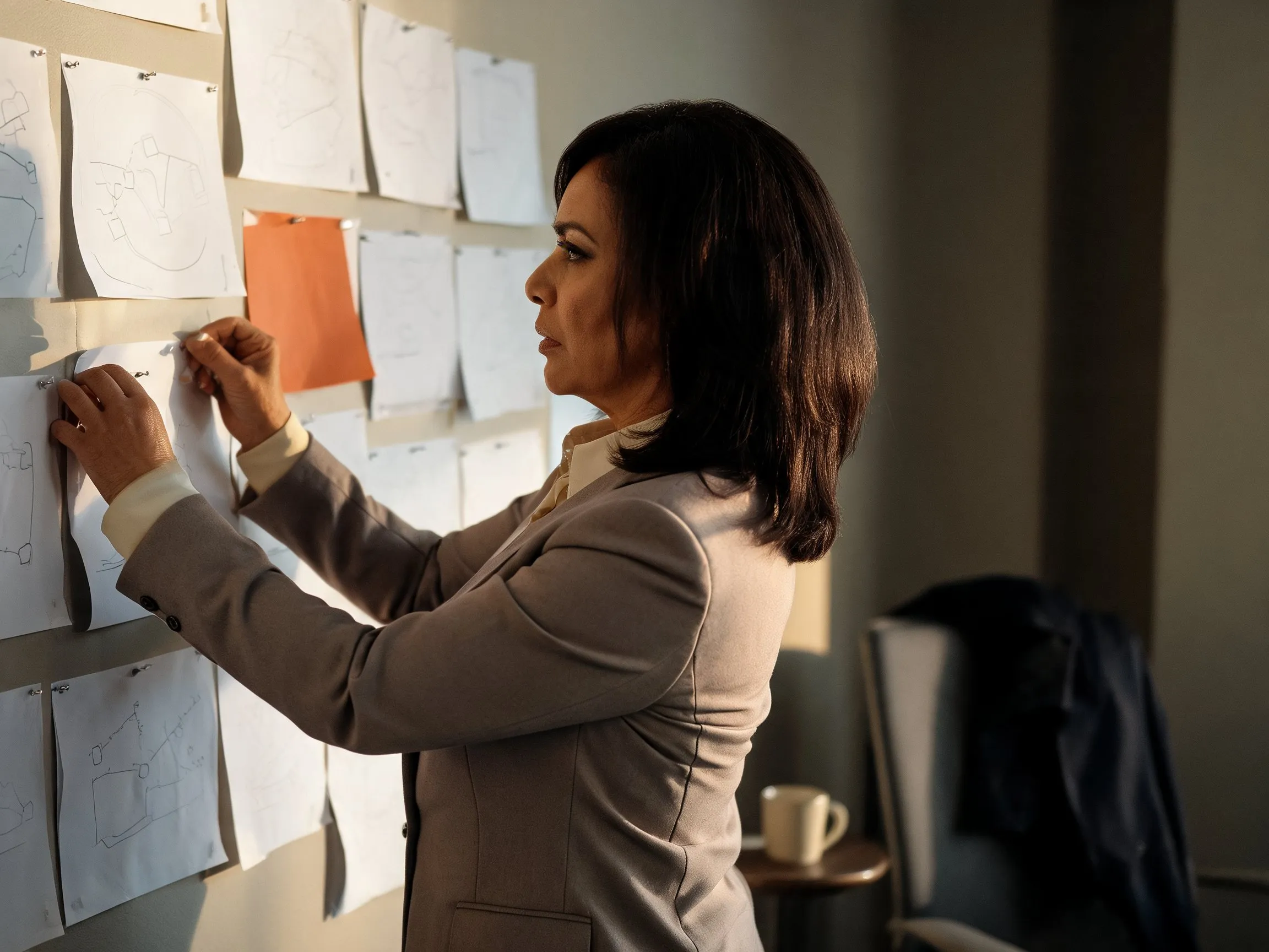 An operator repositioning a sheet on a wall of pinned system diagrams, one flagged in orange.