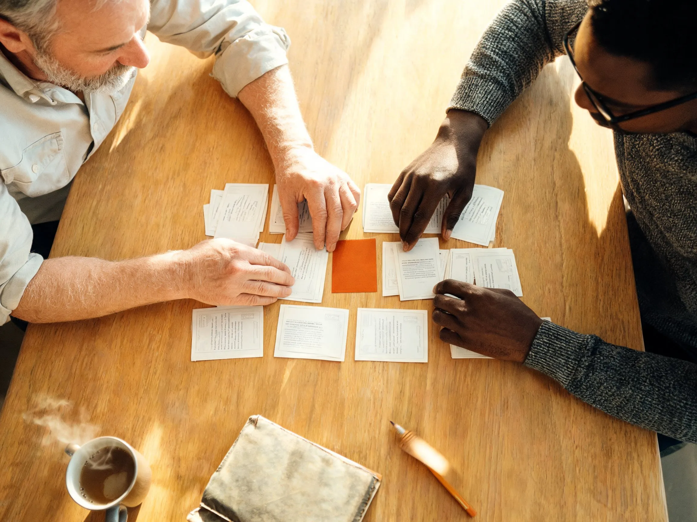 Two colleagues arranging printed process cards into a shared sequence on a sunlit table.